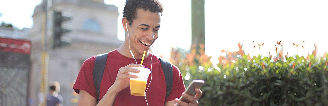 Young man outside listens to mobile phone on ear buds