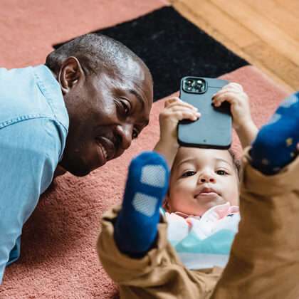 Granddad and baby lay on a rug and look at a mobile screen