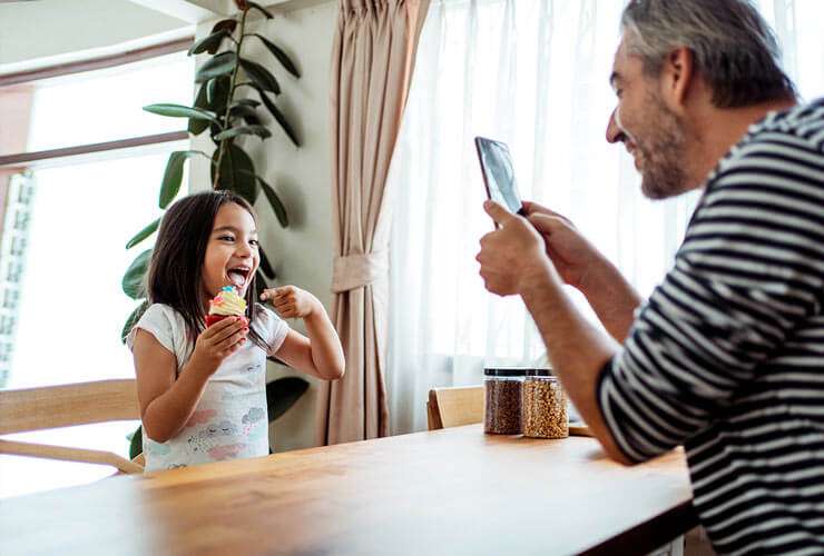 Dad taking a picture of his daughter holding a cupcake