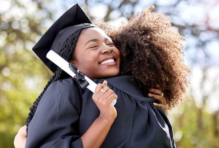 two graduates holding diplomas hug